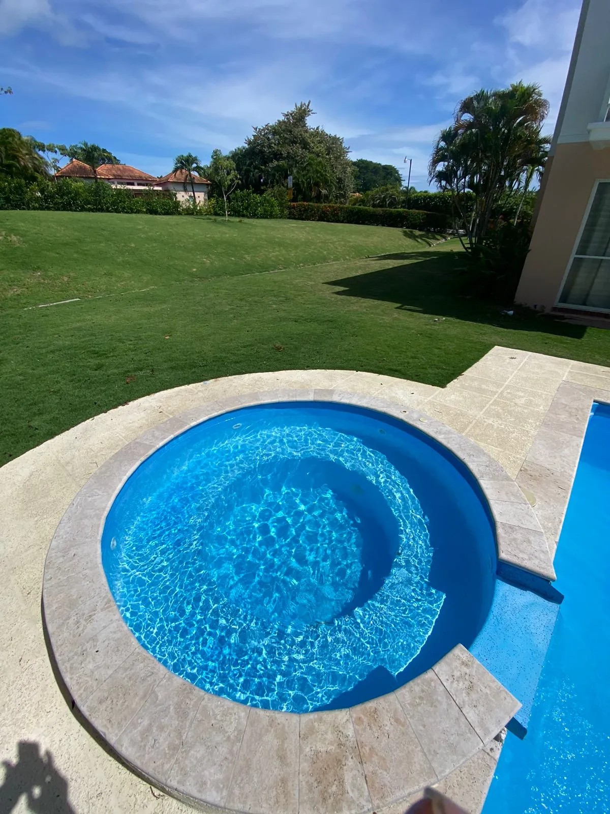 Jacuzzi redondo integrado a piscina residencial con borde de travertino
